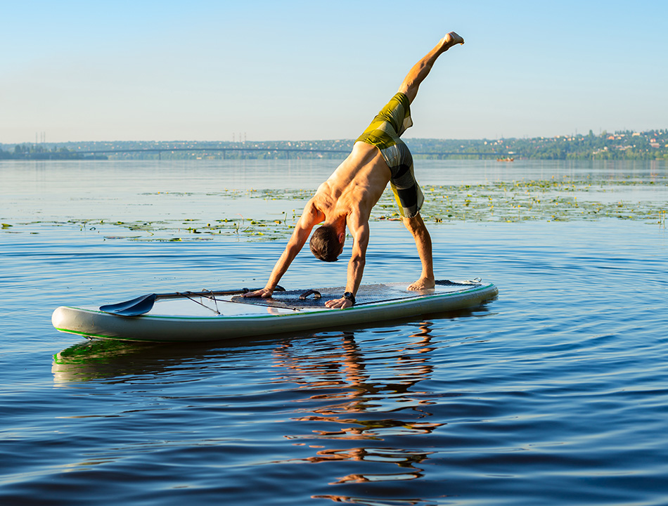 Homme sur un paddle sur un lac en position de yoga représentant la démarche écologique et écoresponsable de CapRol